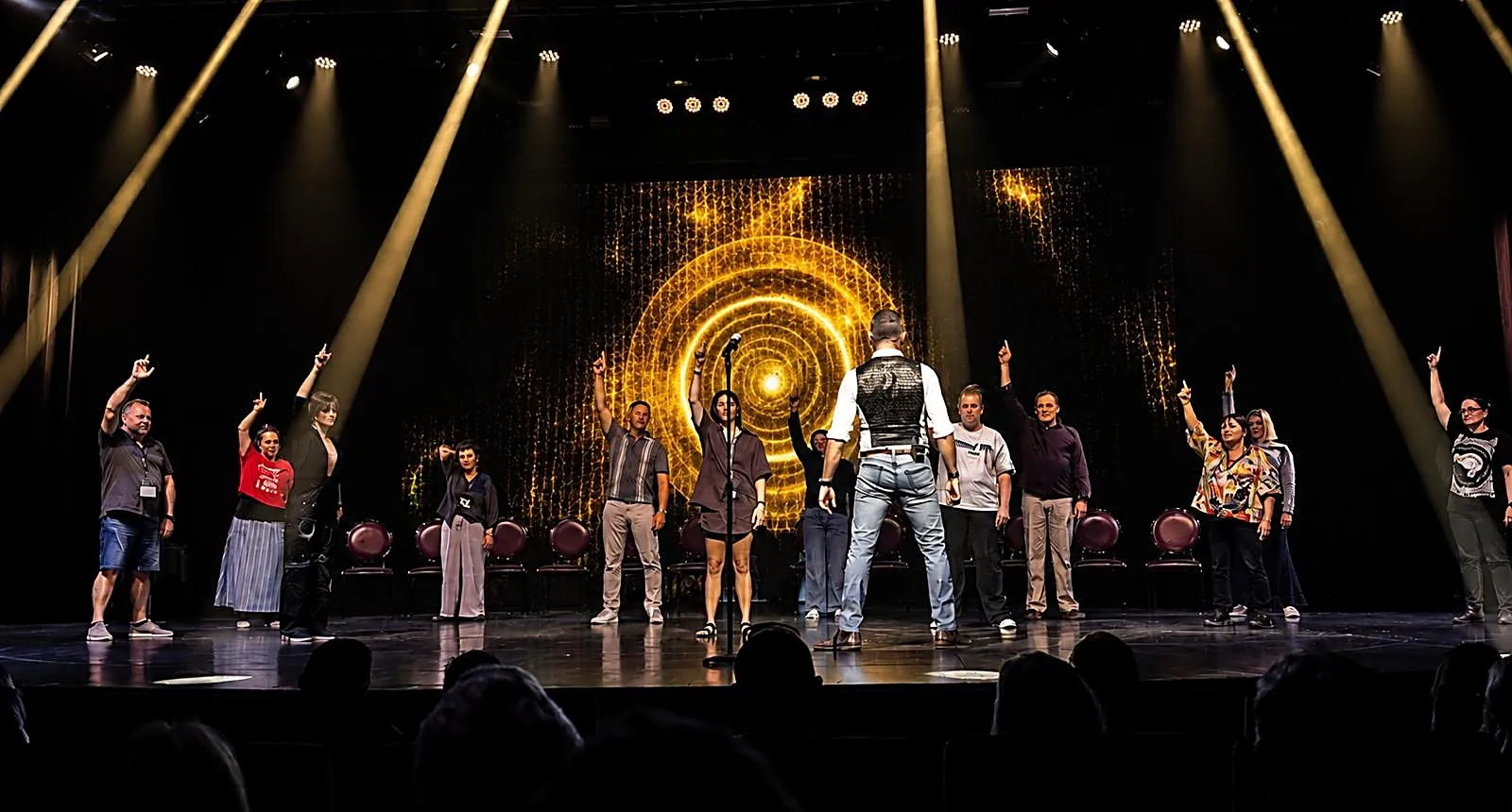 A theatre of volunteers under hypnosis, arms raised, a golden spiral on the stage screen behind them
